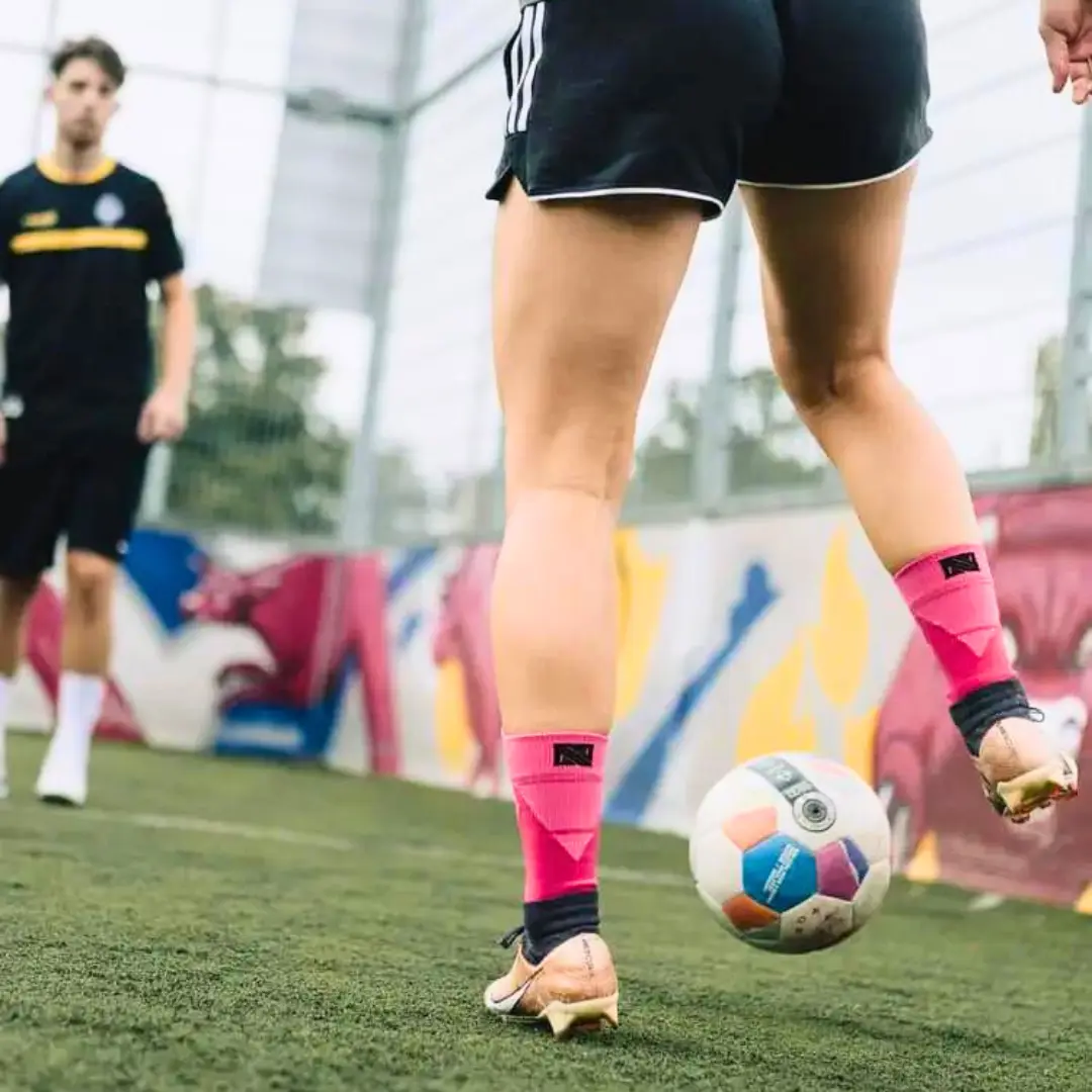 Grip Socken in pinker Farbe. Fußballspielerin dribbelt auf dem Fußballplatz.